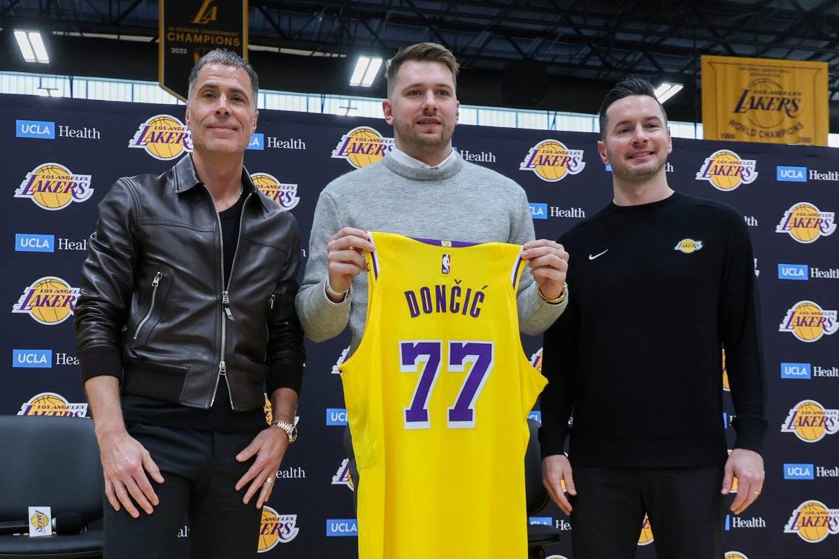 Luka Doncic holds up his new Lakers' threads, alongside general manager Rob Pelinka and head coach JJ Redick.